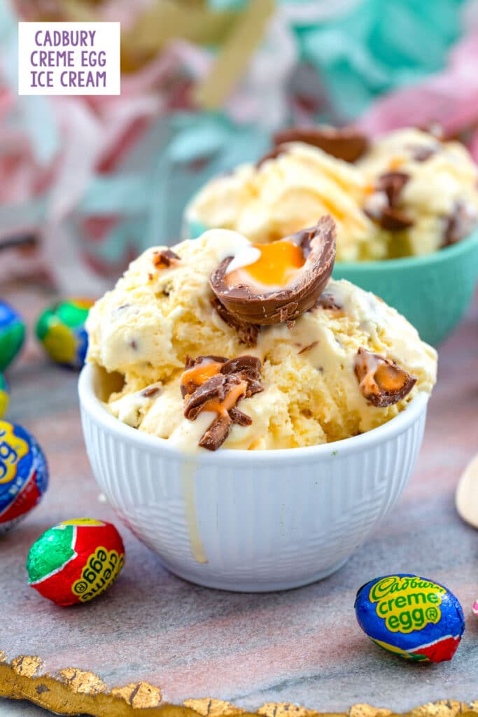 Head-on view of a white bowl of Cadbury Creme Egg ice cream topped with Cadbury Eggs and surrounded by wrapped Cadbury Eggs with second bowl of ice cream in background and recipe title at top
