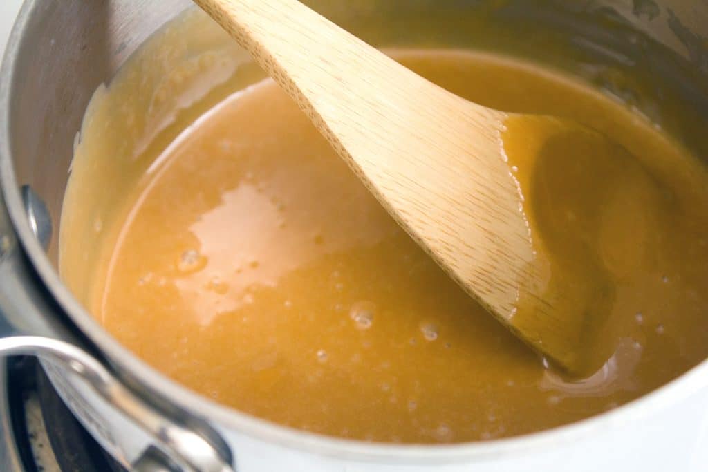 Homemade caramel sauce being stirred in saucepan with a wooden spoon