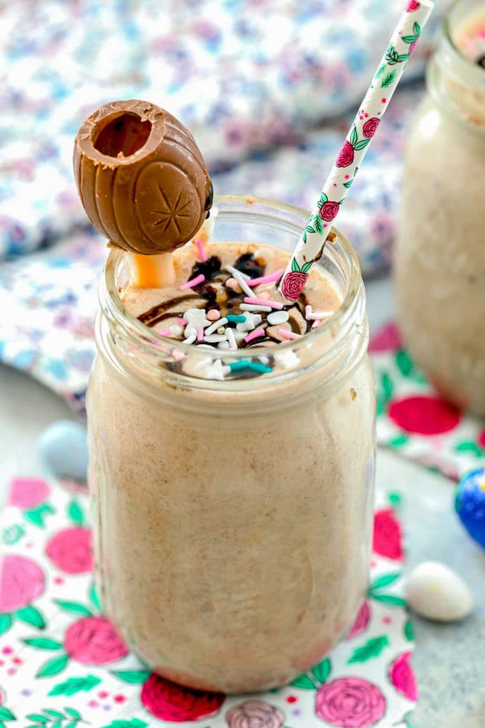 Head-on view of a Cadbury Egg milkshake in a mason jar topped with sprinkles, a Cadbury Cream Egg, and straw