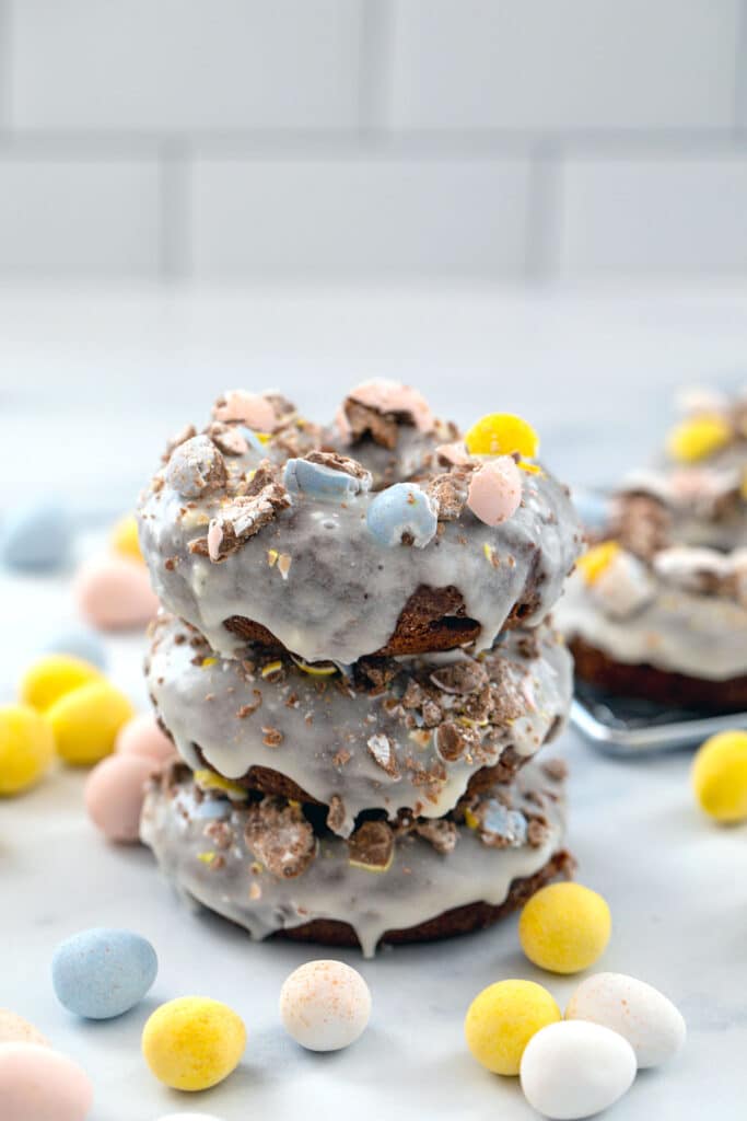 Stack of three Cadbury Mini Egg donuts with Mini Eggs all around and more donuts in background
