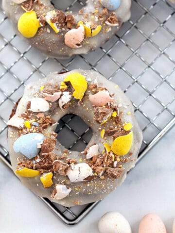 Overhead view of a chocolate Cadbury Mini Egg donut with vanilla icing and crushed Cadbury Mini Eggs on top and more mini eggs all around