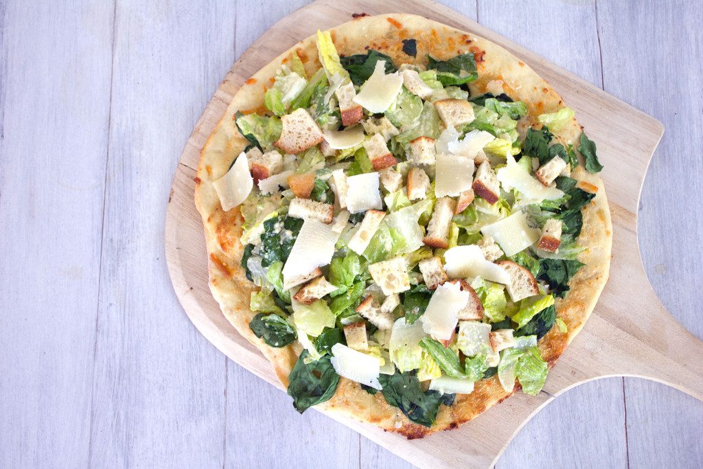 Overhead view of Caesar Salad Pizza on a pizza paddle