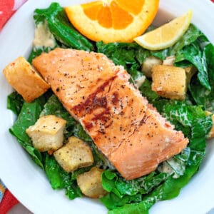 Overhead view of a caesar salad with croutons, an orange wedge, and a lemon wedge, and a piece of grilled salmon
