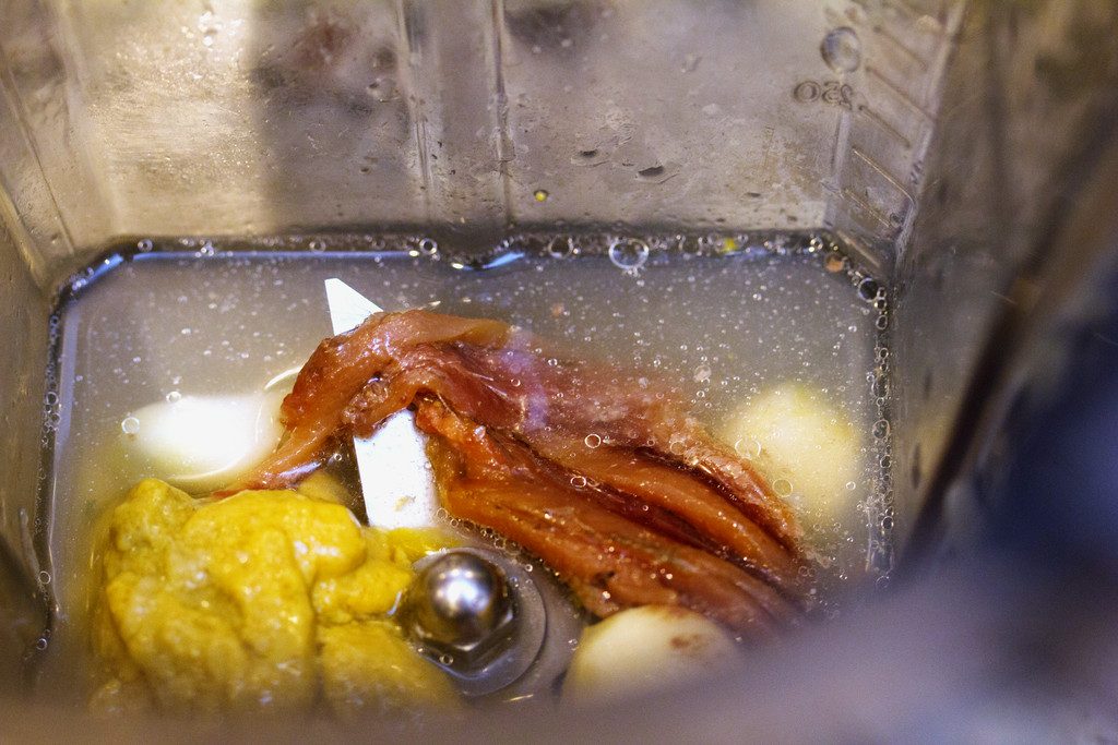 Overhead view of ingredients for caesar dressing in blender, including anchovies, lemon juice, mustard, and garlic