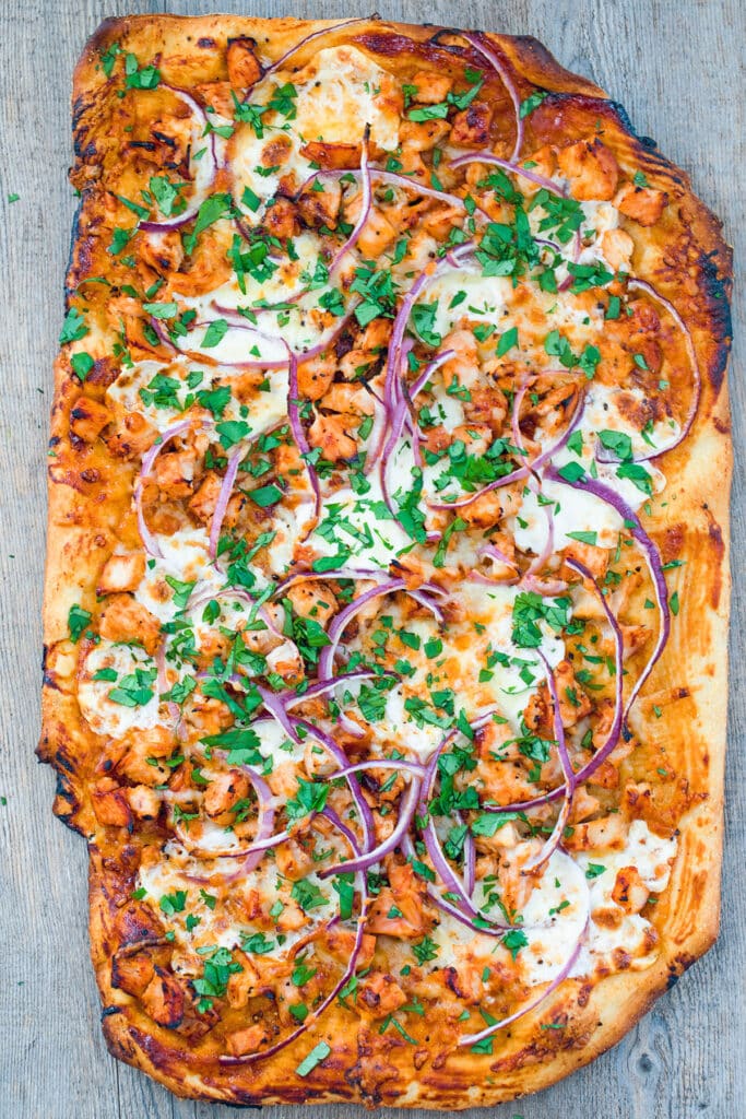 Bird's eye view of BBQ chicken pizza just out of the oven topped with BBQ sauce, chicken, cheese, red onion, and cilantro.