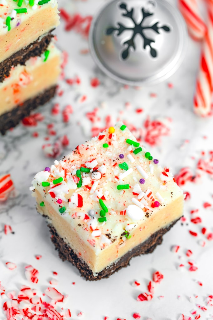 Overhead closeup view of a candy cane cookie dough bar with stack of bars, Christmas bells, and candy canes in the background.