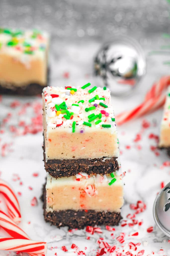 Head-on view of a stack of two candy cane cookie dough bars surrounded by mini candy canes, crushed candy canes, and Christmas bells