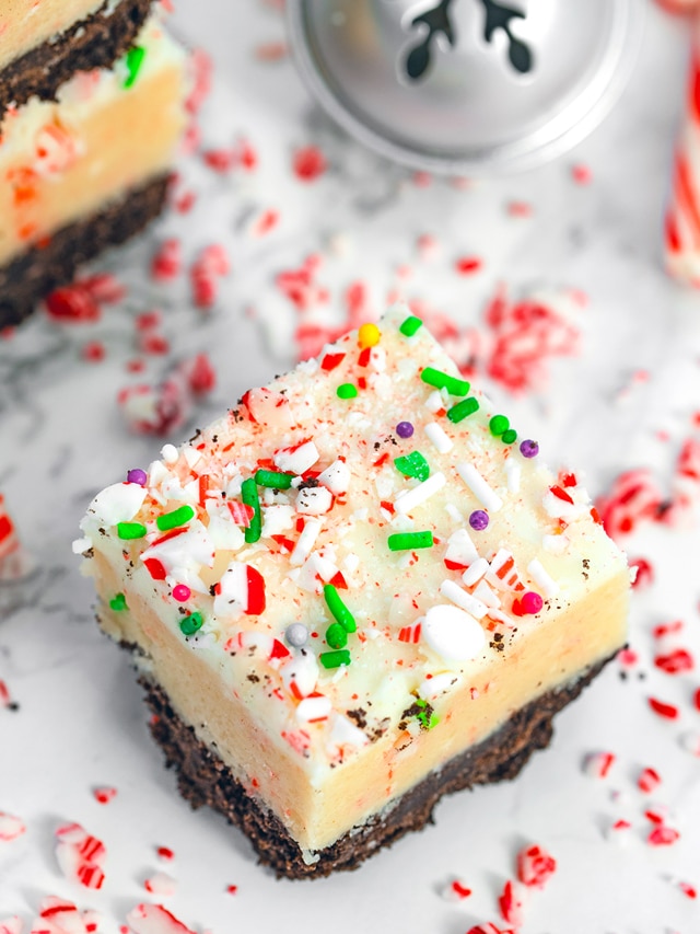 Overhead closeup view of a candy cane cookie dough bar with stack of bars, Christmas bells, and candy canes in the background.