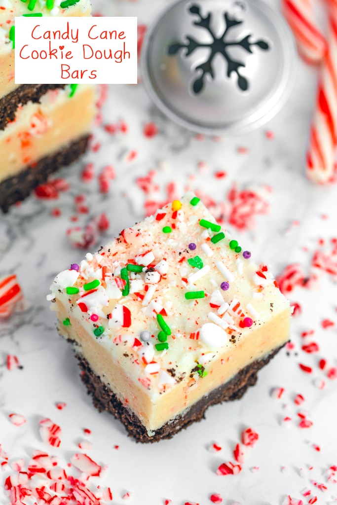 Overhead closeup view of a candy cane cookie dough bar with stack of bars, Christmas bells, and candy canes in the background with recipe title at top.