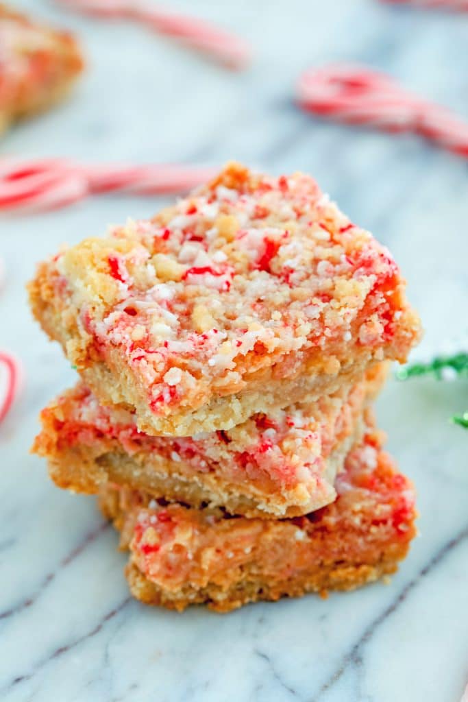 Overhead view of three candy cane crumble bars stacked on top of each other on a marble surface with mini candy canes in the background