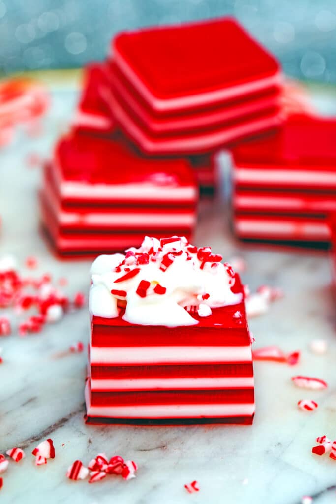Head-on view of a red and white layered candy cane jello shot topped with whipped cream and crushed candy canes with more jello shots in the background.