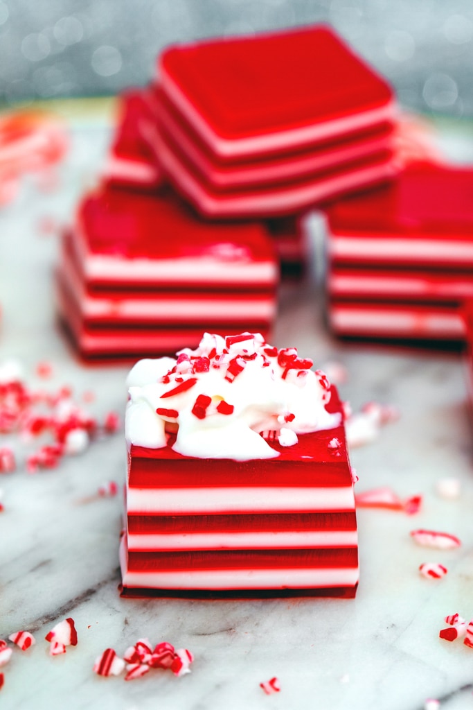 Head-on view of a red and white layered candy cane jello shot topped with whipped cream and crushed candy canes with more jello shots in the background.