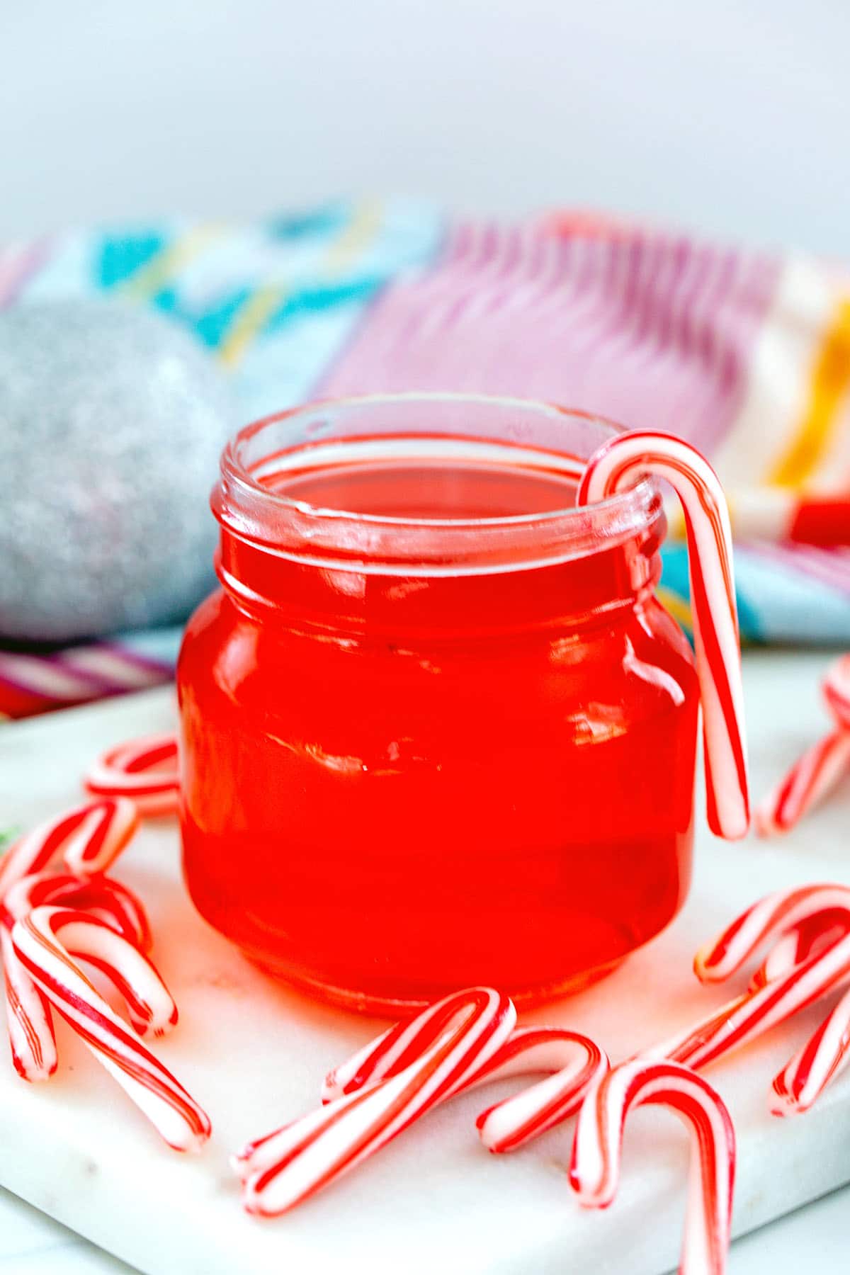 Head-on closeup view of a small jar of candy cane syrup with mini candy canes all around