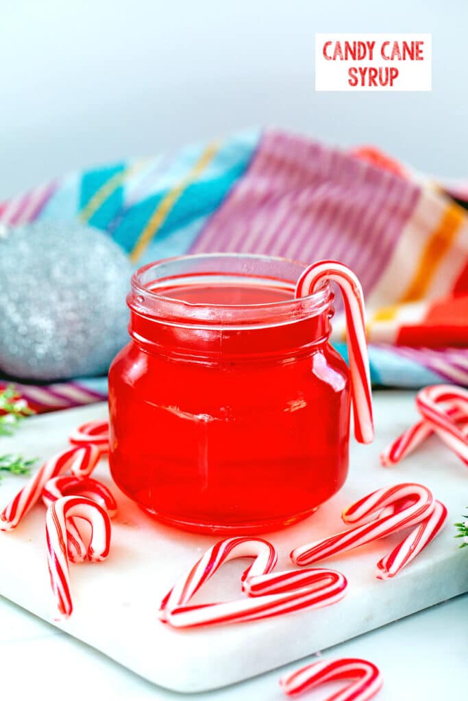 Head-on view of a small jar of candy cane syrup with mini candy canes all around and recipe title at top.