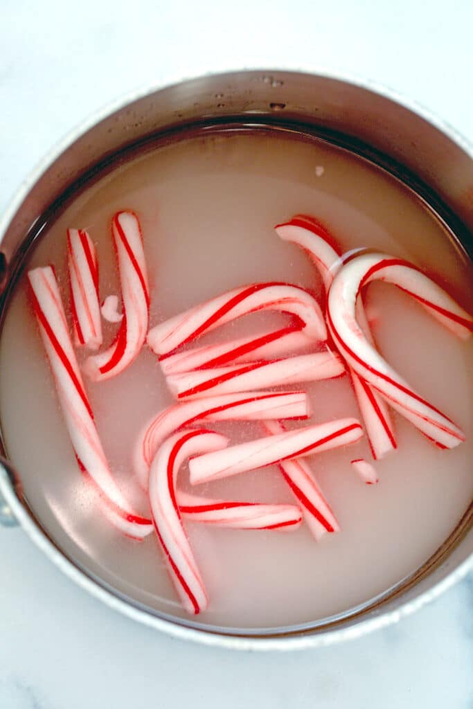 Mini candy canes simmering in sugar and water in saucepan.