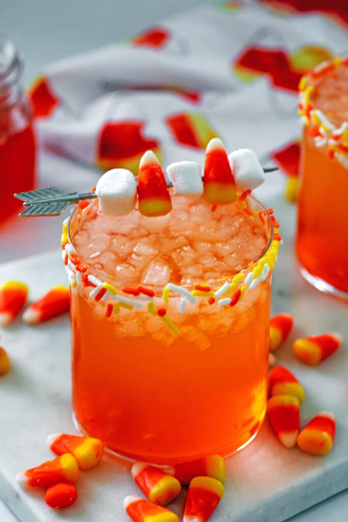 Candy corn cocktail with candy corn and marshmallow garnish and candy corns all around