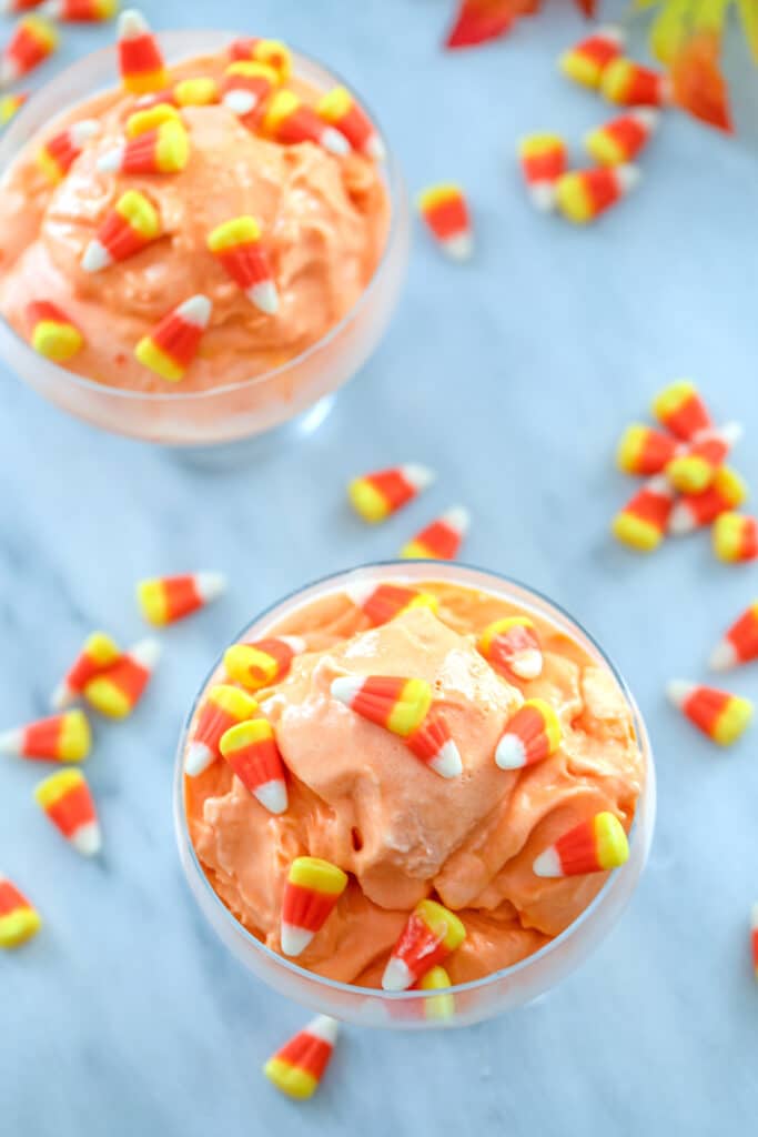Bird's eye view of two clear dishes of orange candy corn ice cream topped with candy corn with candy corn scattered all around