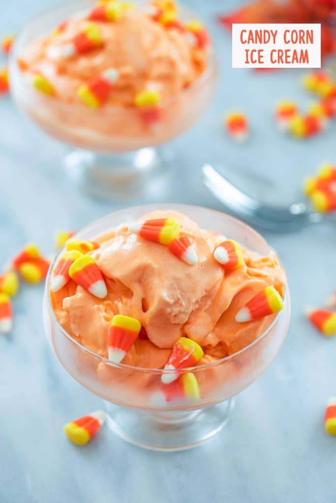 Overhead view of clear bowl of candy corn ice cream surrounded by candy corn, a spoon, and second bowl of ice cream in the background with "Candy Corn Ice Cream" text at top