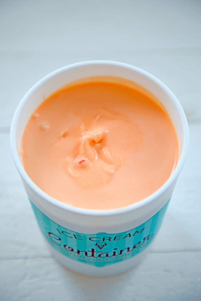 Quart-size ice cream container filled with orange ice cream before it's fully frozen