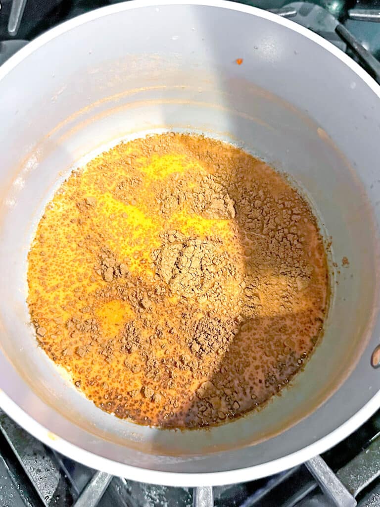 Candy corn hot chocolate with cocoa powder in saucepan.
