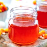 Up-close view of a small mason jar of bright orange candy corn simple syrup with candy corn all around