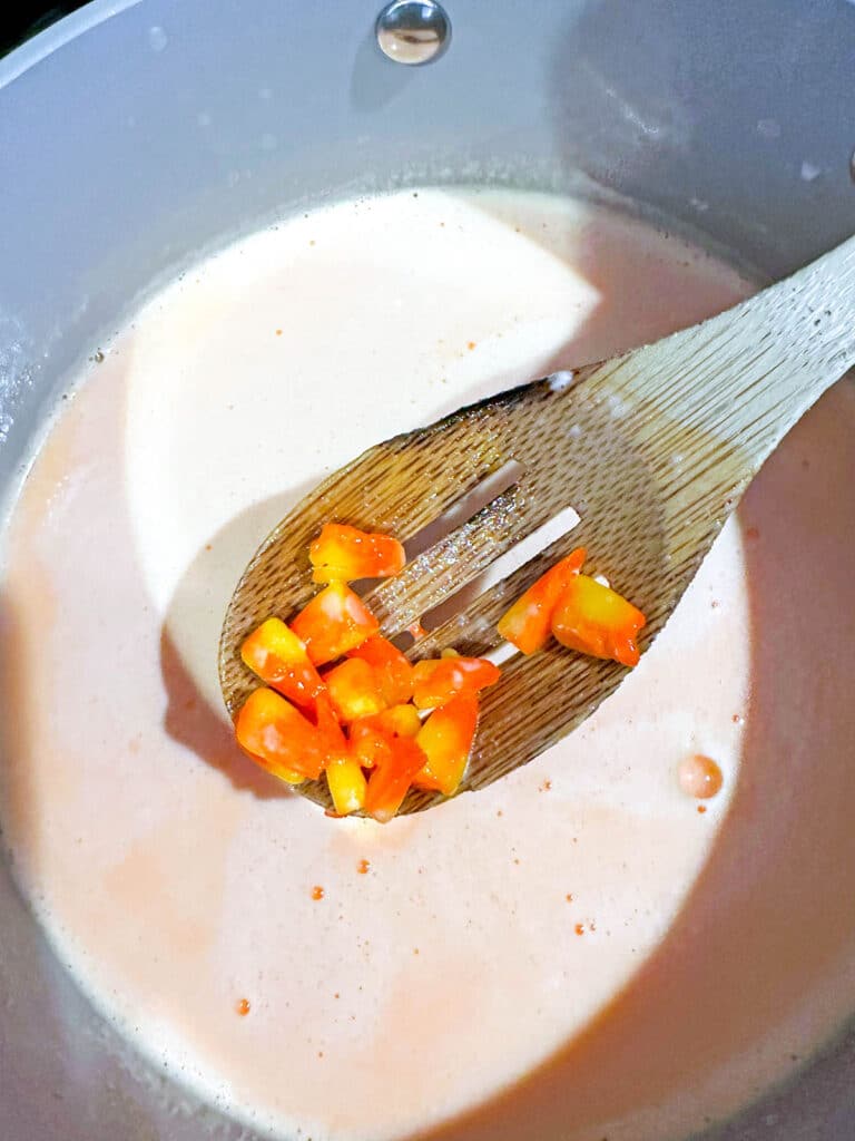 Milk in saucepan with candy corn disintegrating into it.