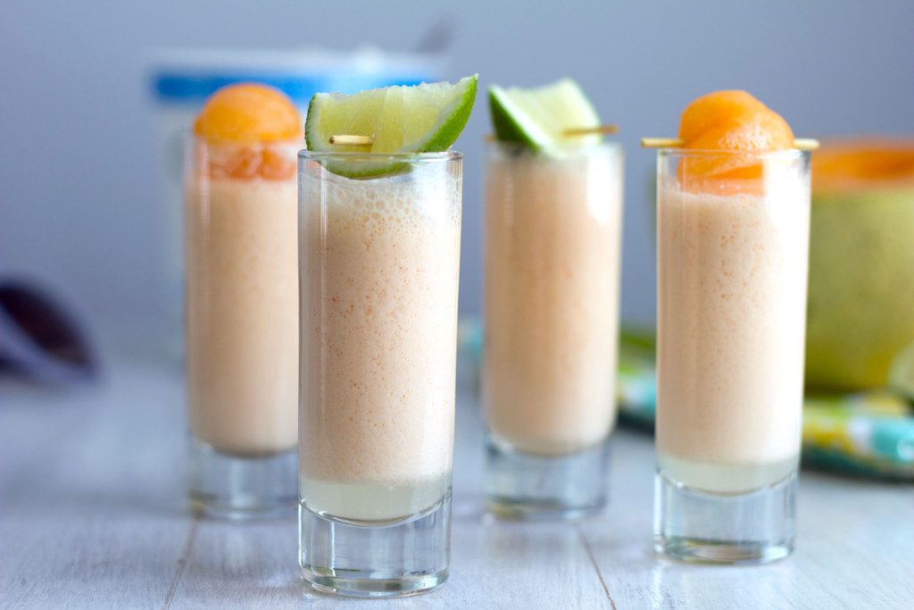 Landscape view of multiple cantaloupe boozy smoothie shooters with cantaloupe and lime garnishes