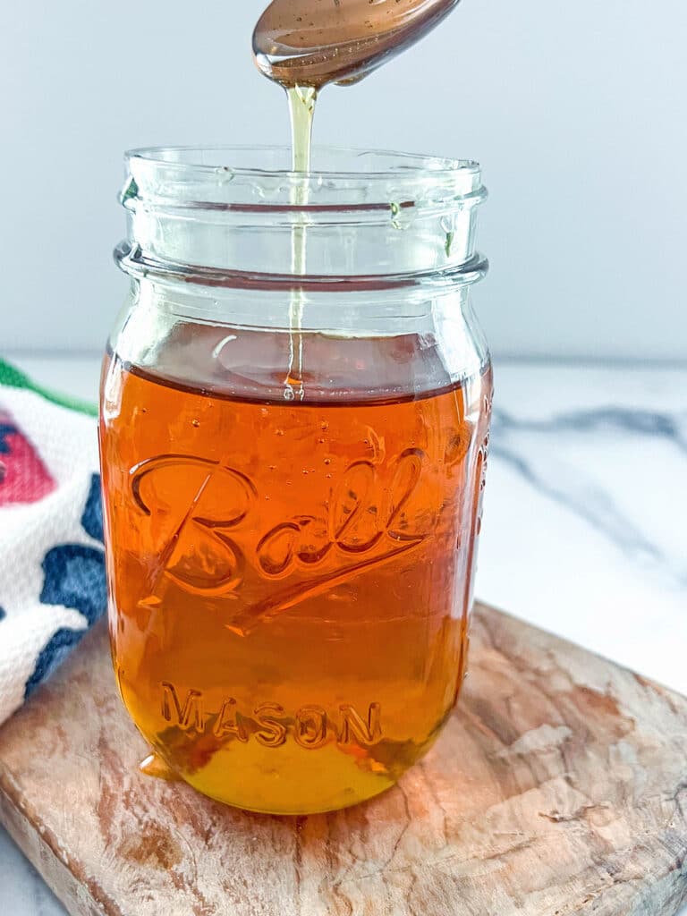 Head-on view of a mason jar of caramel syrup with a spoon over it drizzling syrup into it.
