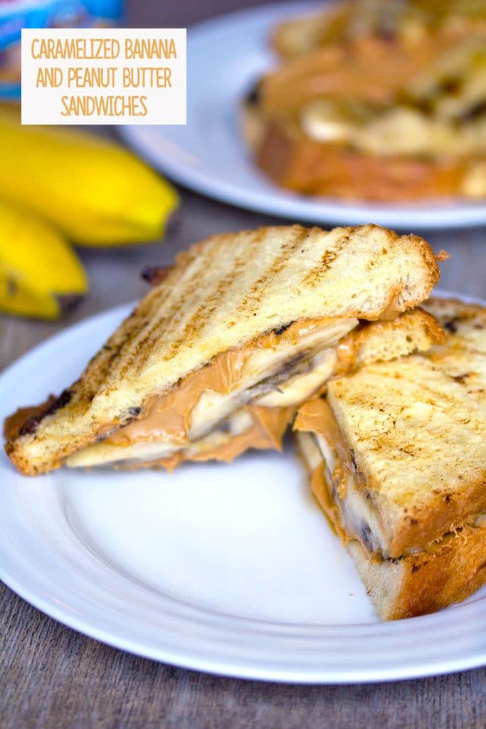 Head-on view of a caramelized banana and peanut butter sandwich cut in half on a white plate with a second sandwich, bananas, and peanut butter jar in the background and recipe title at the top