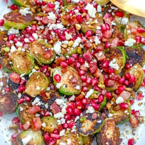 Overhead closeup view of caramelized brussels sprouts with pancetta, pomegranate, and feta on a white platter