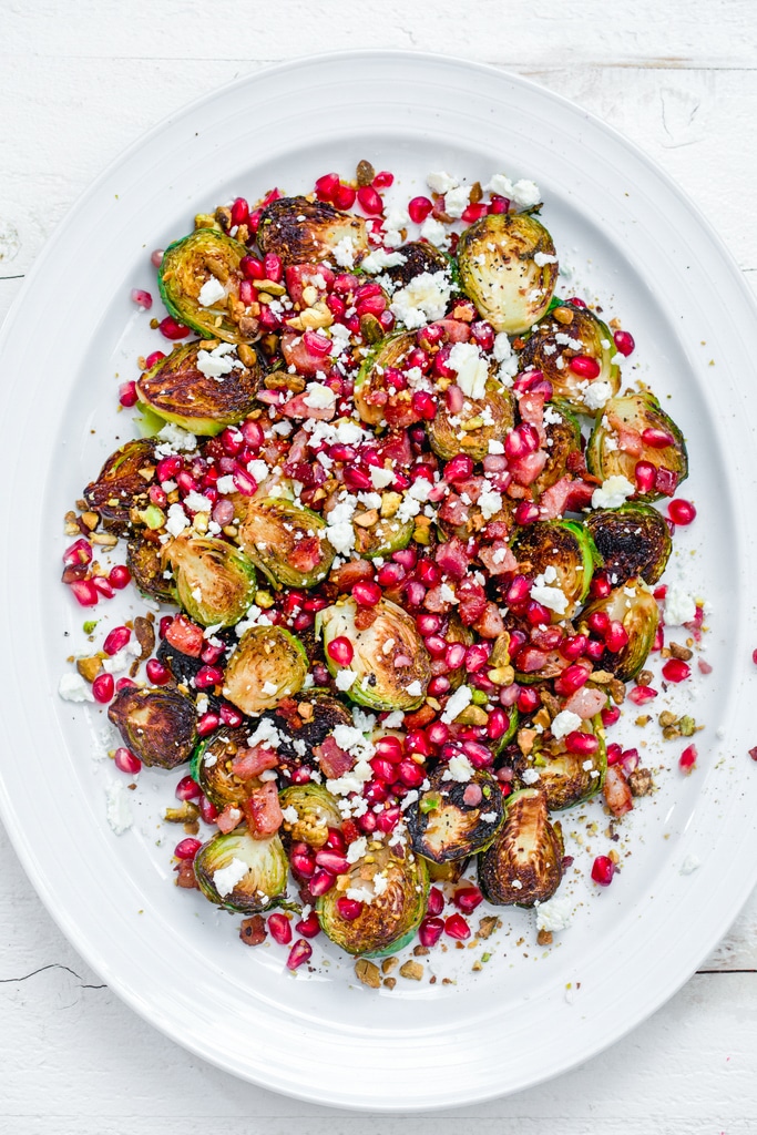 Bird's eye view of a white platter with caramelized brussels sprouts with pancetta, pomegranate, and feta