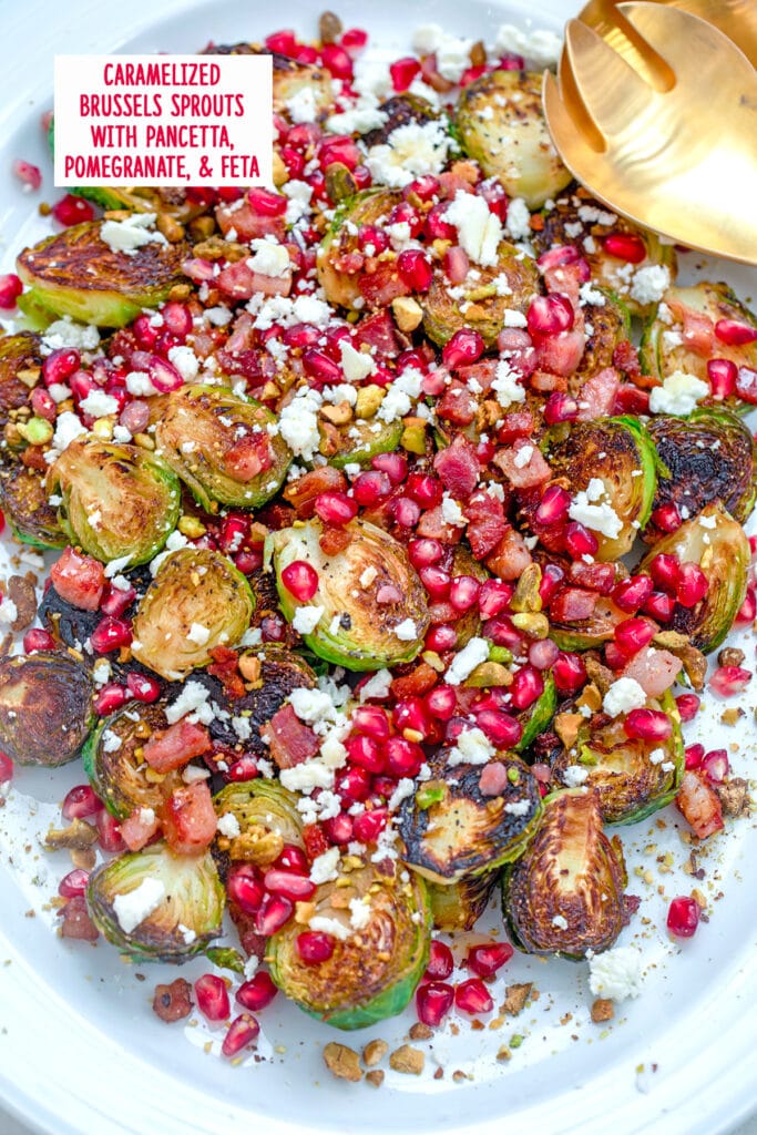 Overhead view of caramelized brussels sprouts with pancetta, pomegranate, and feta on a white platter with gold serving pieces and recipe title at top