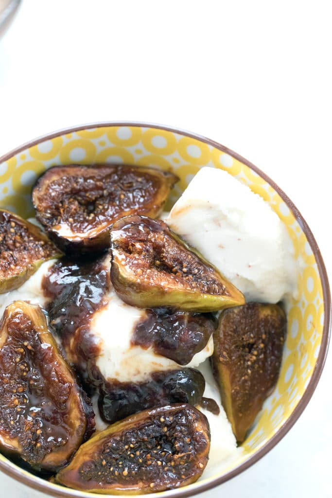 Overhead view of a yellow bowl filled with vanilla ice cream and topped with caramelized figs along with some of their juices