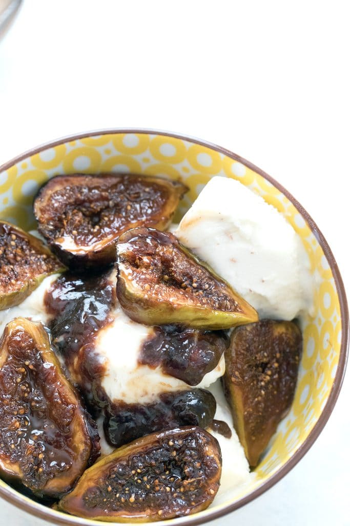 Overhead view of a yellow bowl filled with vanilla ice cream and topped with caramelized figs along with some of their juices