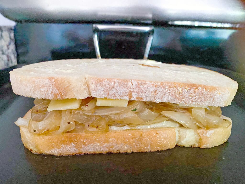 Head-on view of a french onion grilled cheese sandwich cooking on a skillet
