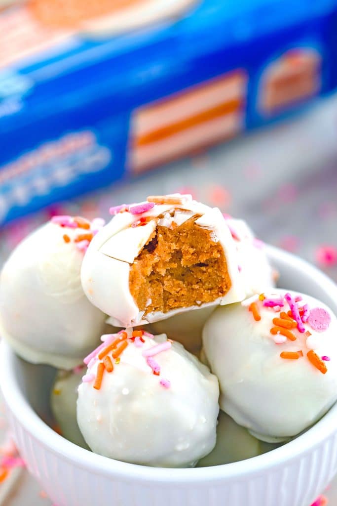 Closeup head-on view of Carrot Cake Oreo truffles in a bowl with a bite taken out of the top one and package of cookies int he background