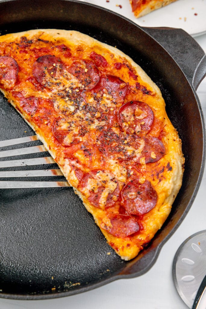 Half of a pizza in a cast iron skillet with spatula.