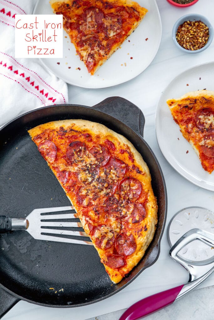 Overhead view of half a cast iron skillet pizza with slices on plates on the side, pizza cutter, and red pepper flakes with recipe title at top.