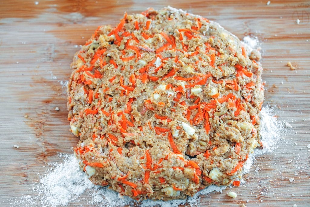 Overhead view of chai carrot cake scone dough mounded into a 3/4" thick mound on a wood cutting board ready for cutting