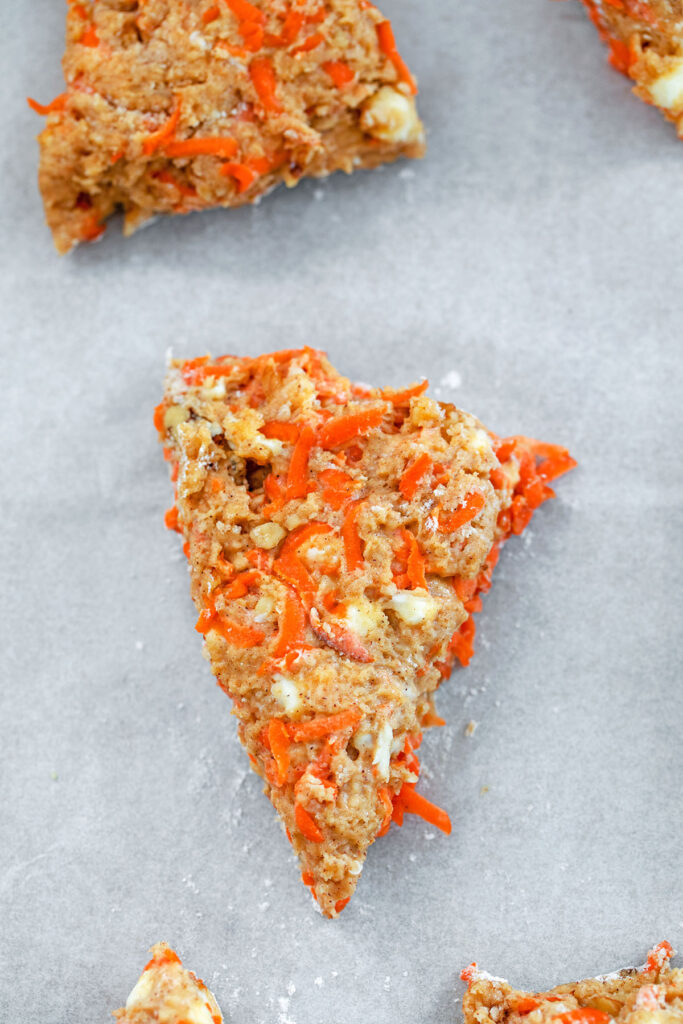 Chai carrot cake scone wedges on a parchment paper lined baking sheet ready for baking