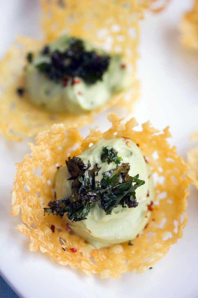 Overhead closeup view of a cheddar cup filled with avocado feta mousse and topped with crispy kale