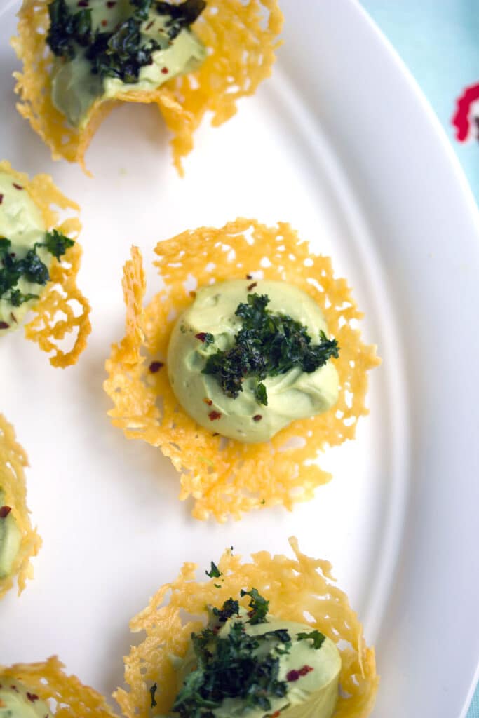 Overhead view of cheddar cups filled with avocado feta mousse and crispy kale on a white platter