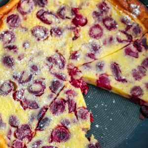 Overhead view of cherry clafoutis in skillet with slice taken out and "Cherry Clafoutis" text at top