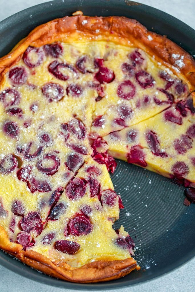 Overhead view of cherry clafoutis in skillet with slice taken out