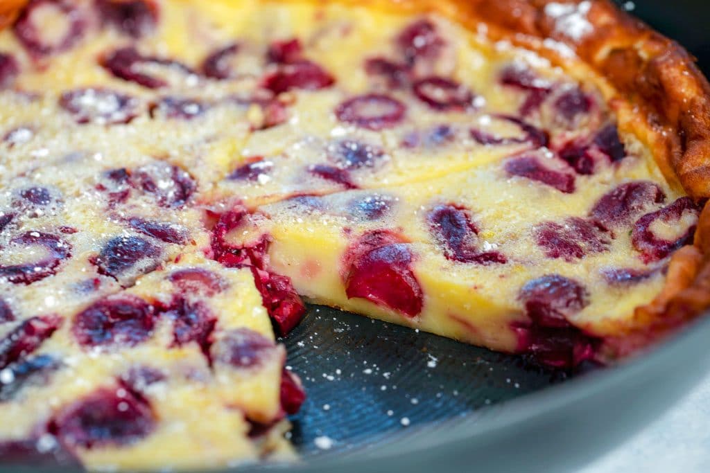 Landscape up-close view of slice taken out of cherry clafoutis in skillet 