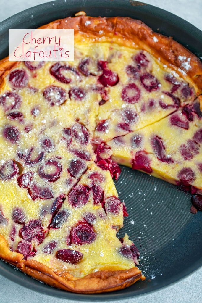 Overhead view of cherry clafoutis in skillet with slice taken out and "Cherry Clafoutis" text at top