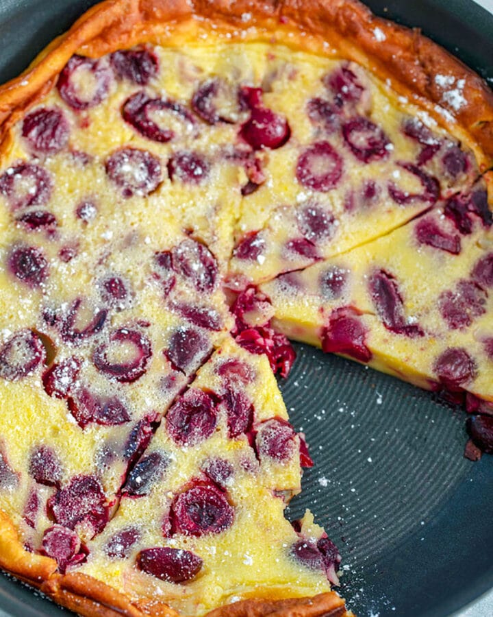 Overhead view of cherry clafoutis in skillet with slice taken out