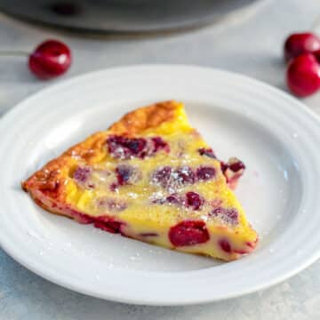 Closeup view of a slice of cherry clafoutis on a white plate.
