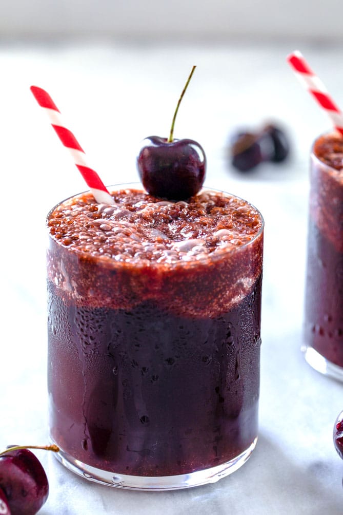 Closeup head-on view of a glass of cherry Coke and rum with a red and white striped straw and cherry garnish