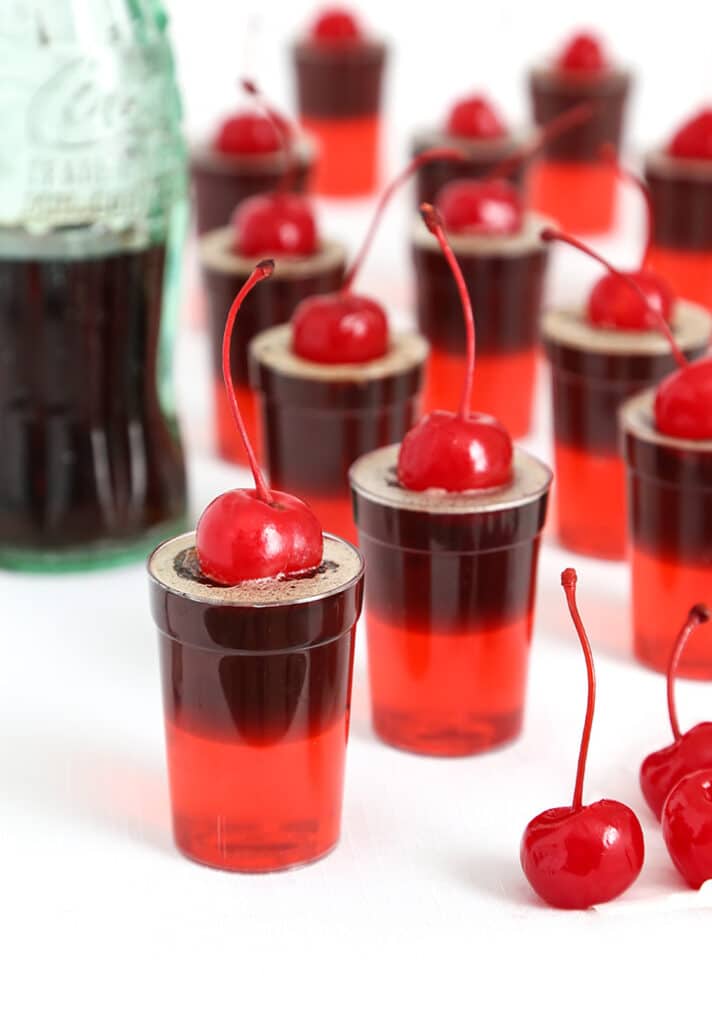 Cherry cola jello shots in little cups with maraschino cherry garnish